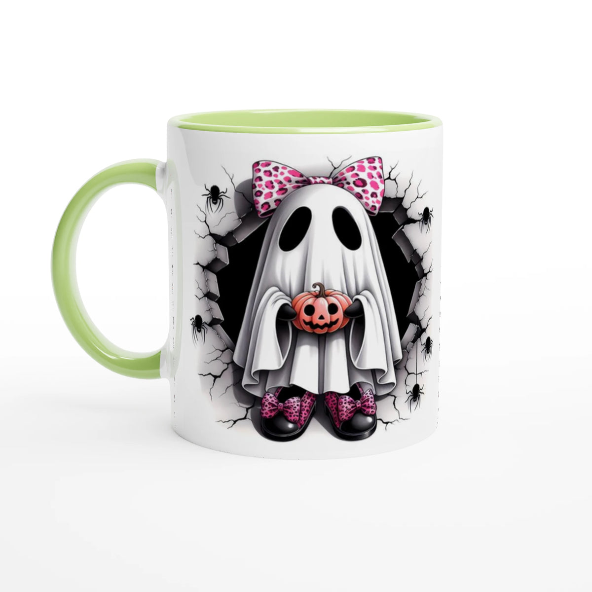 White mug with light green handle and interior, featuring a ghost with a pink spotted bow holding a jack-o’-lantern, surrounded by cracked stone and spiders